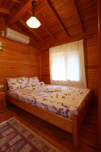 a bed in a wooden room with a window at Olympos Doga Pansiyon in Olympos