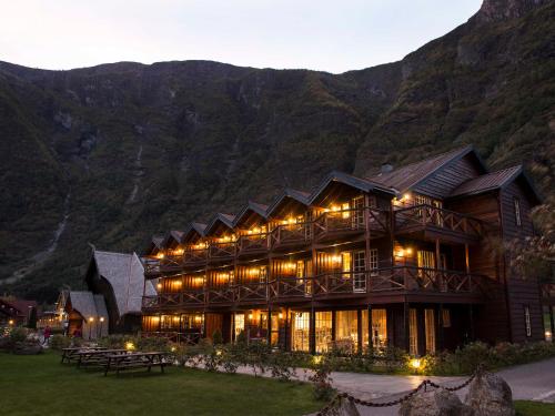 a large wooden building with mountains in the background at Flåmsbrygga Hotel in Flåm