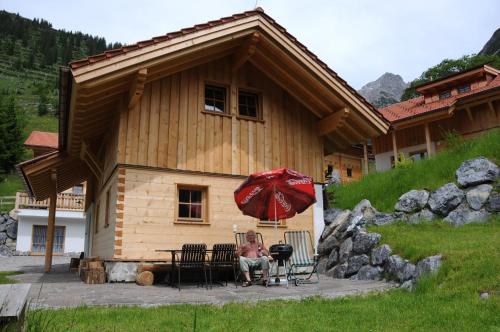 a woman sitting under an umbrella in front of a cabin at Lechtaler Naturparkchalets in Gramais