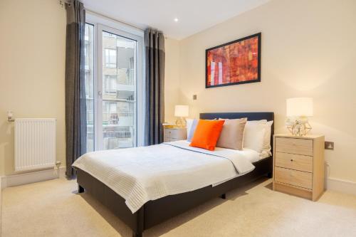 a bedroom with a bed with orange pillows and a window at Two Bedroom Apartments in Limehouse in London