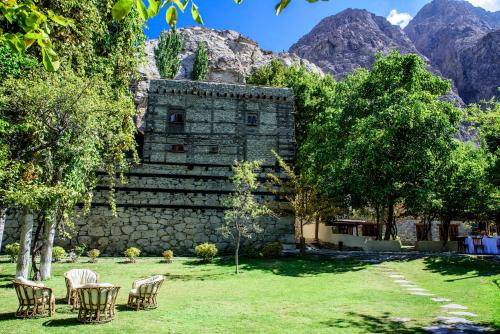 a stone building with chairs and trees and mountains at Serena Shigar Fort in Shigar