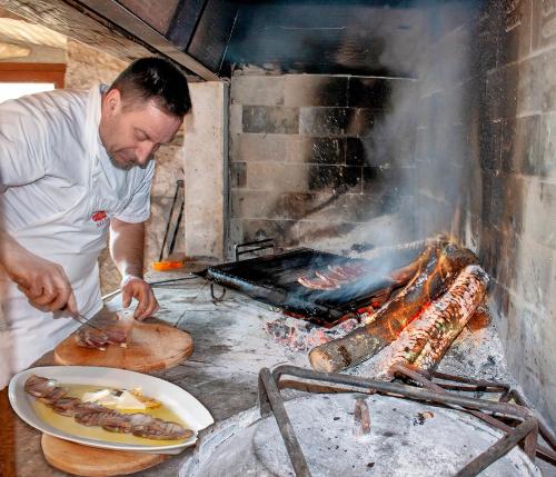 a man cooking food in front of a grill at Rooms Agroturizam Romano in Buje