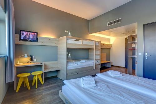 a bedroom with two beds and a desk and two stools at MEININGER Hotel Berlin Airport in Berlin