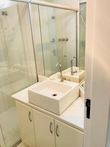 a white bathroom with a sink and a shower at 6 Flats Capitania Varan, Pitangueiras, wifi in Guarujá