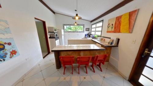 a kitchen with a counter and four red chairs at Casa do Joca - Ilhabela in Ilhabela