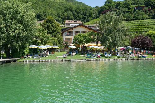 a lake with chairs and umbrellas next to a building at PENSION KLUGHAMMER in Caldaro