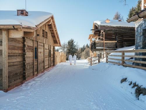 two people walking in the snow next to a cabin at Rifugio Graziani Hütte in San Vigilio Di Marebbe