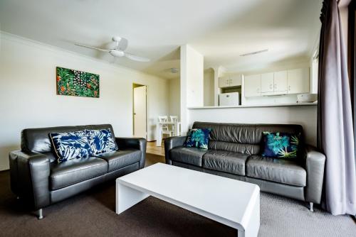 a living room with two leather couches and a table at Coffs Harbour Holiday Apartments in Coffs Harbour