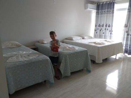 a boy standing in a room with two beds at Pousada Vó Santina in Protásio Alves