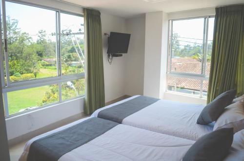 a bedroom with two beds and a tv and windows at Llanogrande Airport by Bernalo Hotels in Rionegro