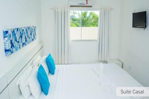 Habitación blanca con almohadas azules y ventana en Porto Seguro. Residencial Monte Hebron ., en Porto Seguro