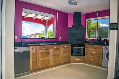 a kitchen with purple walls and wooden cabinets at VILLA D'ALICE 1 in Sainte-Anne