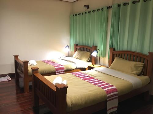 two beds in a room with green curtains at Baan Mai Muang Nan in Nan