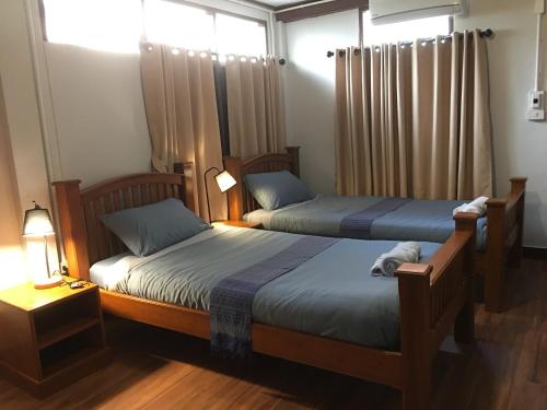 two beds in a bedroom with two lamps and curtains at Baan Mai Muang Nan in Nan