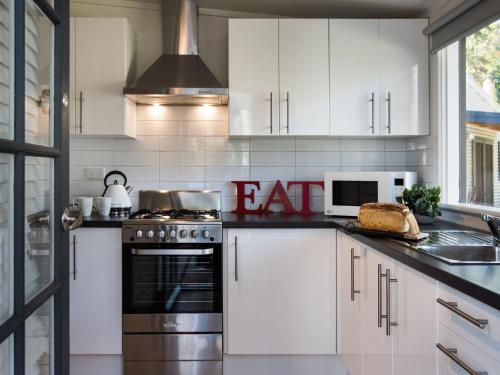 a kitchen with white cabinets and a stove top oven at Gumnut Cottage Daylesford in Daylesford