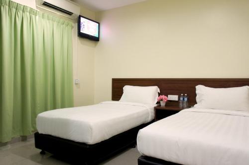 two beds in a room with a green curtain at Maple Inn in Kuala Lumpur