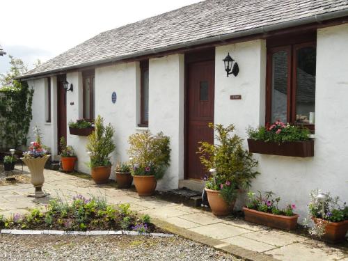 a white house with potted plants in front of it at Shegarton Farm Cottages in Luss