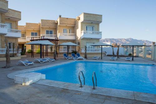 a pool in front of a building with chairs and umbrellas at Dahab Hotel in Dahab