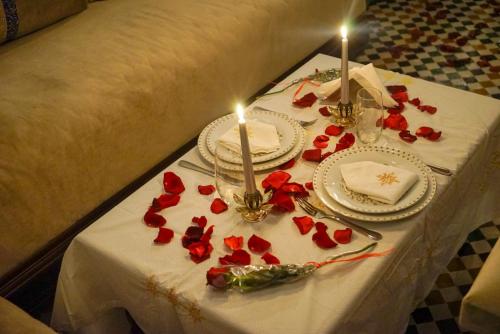 a table with plates and candles and red roses on it at Le Grand Alcazar - Riad in Fès