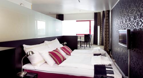a bedroom with a bed with white sheets and a television at Home Hotel Arcticus in Harstad