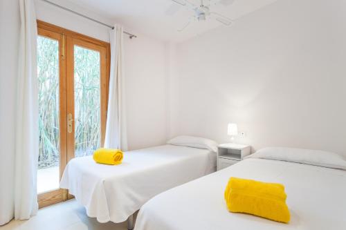 two beds in a white room with yellow towels on them at APARTAMENTO EL ROJO in Can Picafort