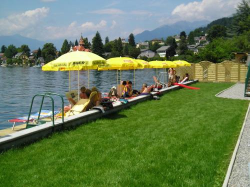 a group of people sitting under umbrellas on the water at Hotel Posthof in Millstatt