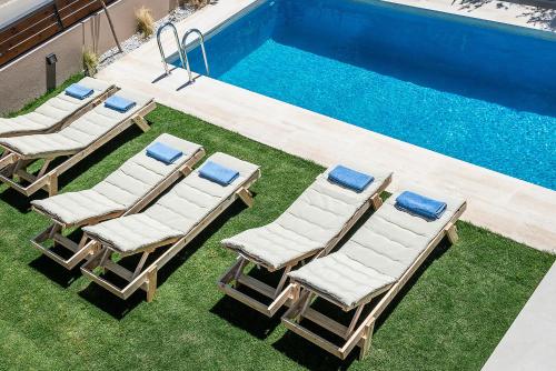 a group of lounge chairs next to a swimming pool at Fos Villa, a Luxe House with Private Heated Pool in Galatás
