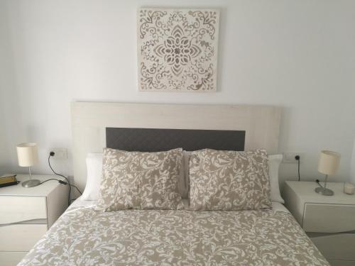 a white bedroom with a bed with two tables and two lamps at Piso Con Terraza y Vistas Espectaculares in Carmona