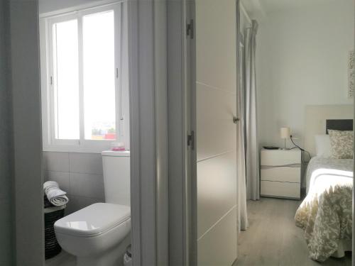 a white bathroom with a toilet and a window at Piso Con Terraza y Vistas Espectaculares in Carmona