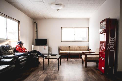 a man sitting on a couch in a living room at Hakuba Cortina Backpackers in Otari