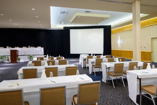 une salle de conférence avec des tables et des chaises blanches et un écran dans l'établissement Metro Points Hotel Washington North, à New Carrollton
