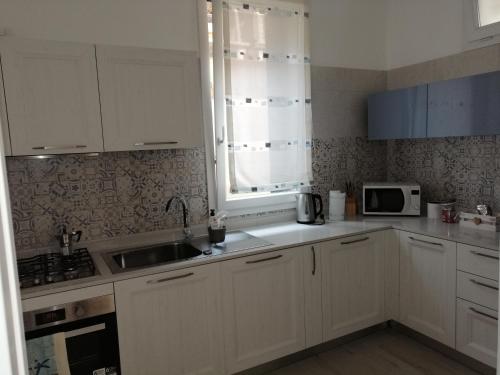 eine Küche mit weißen Schränken, einer Spüle und einer Mikrowelle in der Unterkunft Via Cipro 16 in Lido di Venezia