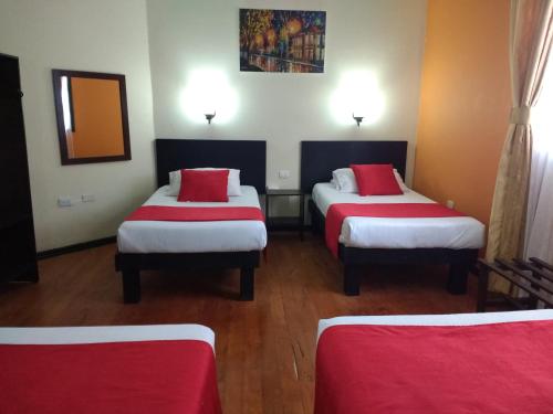 a room with three beds with red and white sheets at Hotel La Herreria Colonial in Popayan