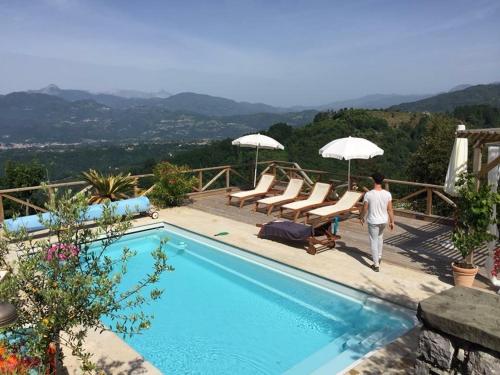 a man walking by a swimming pool with chairs and umbrellas at Villa Colletto in Coreglia Antelminelli