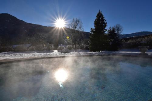 a snow covered yard with a pool with the sun in the background at Majestic - Unique Spa Resort in Brunico