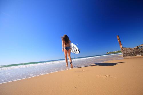 a woman walking on the beach with a surfboard at Portobello By The Sea in Caloundra