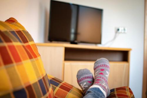 a person sitting on a couch in front of a tv at Ferienwohnungen Lichtenegger in Kamp