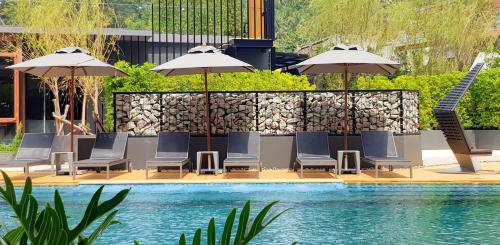 a group of chairs and umbrellas next to a pool at Aurico Kata Resort & Spa - SHA Extra Plus in Kata Beach