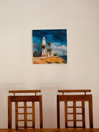 two wooden stools against a white wall with a painting at Serendipity (Weligama) in Weligama