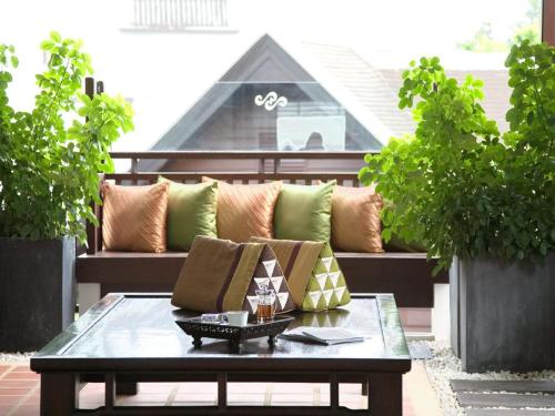 a bench with pillows on a patio with a coffee table at Rarin Jinda Wellness Spa Resort in Chiang Mai
