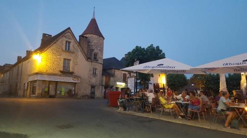 un groupe de personnes assises à des tables devant un bâtiment dans l'établissement AU SOLEIL COUCHANT, à Saint-Julien-de-Lampon