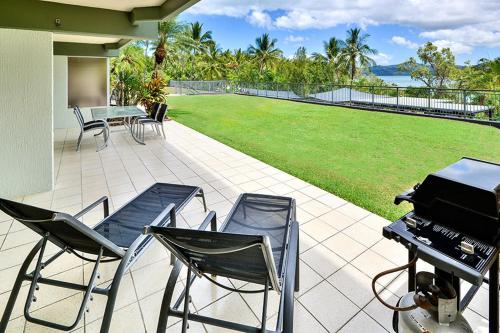 a patio with chairs and a grill and a lawn at Hibiscus 006 - Hamilton Island in Hamilton Island