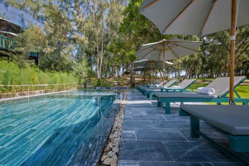 ein Pool mit Liegestühlen und Sonnenschirmen daneben in der Unterkunft Sol An Bang Beach Resort & Spa in Hoi An