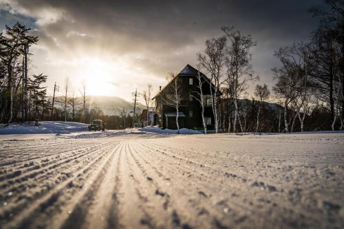 a house in the snow with the sun in the background at Cortina Apartment in Otari