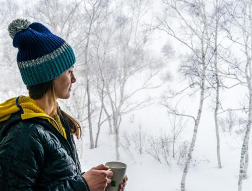 a woman holding a cup of coffee in the snow at Cortina Apartment in Otari