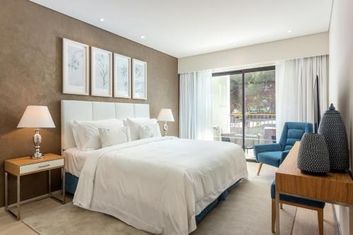 Pine Cliffs Gardens في ألبوفيرا: غرفة نوم بسرير ابيض وكرسي ازرق