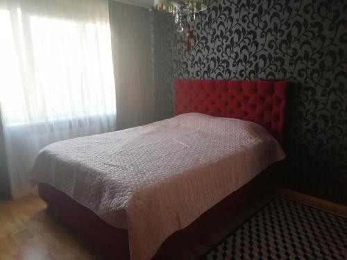 a bedroom with a bed with a red headboard and a window at Justinos Apartamentai Panevėžyje in Panevėžys