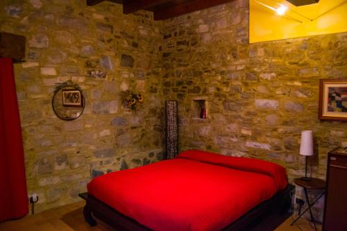 a bedroom with a red bed in a stone wall at L'Angolo Di Verlano in Canossa