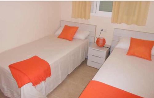 2 Betten mit orangefarbenen Kissen im Schlafzimmer in der Unterkunft Playa Sol Apartment in Denia