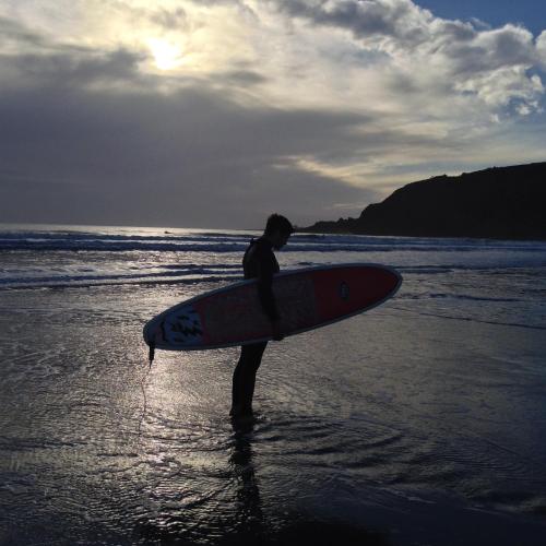 a man standing on the beach holding a surfboard at QUILLET COTTAGE, 2 GLENTOWAN ROAD in St Austell